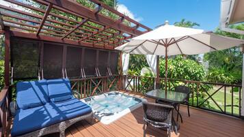 Una terraza de madera con un jacuzzi, una silla de descanso y una mesa con sombrilla.