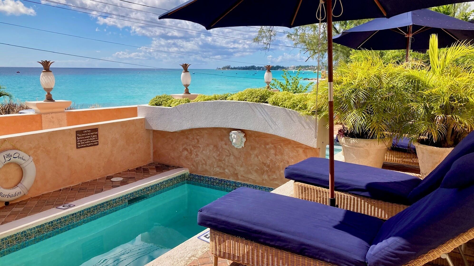 A poolside area with lounge chairs, a pool, and a view of the ocean.