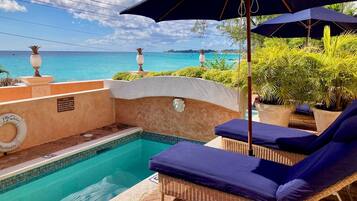 A poolside area with lounge chairs, a pool, and a view of the ocean.