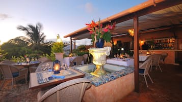 An outdoor dining area with tables, chairs, a decorative fountain, and a bar in the background.