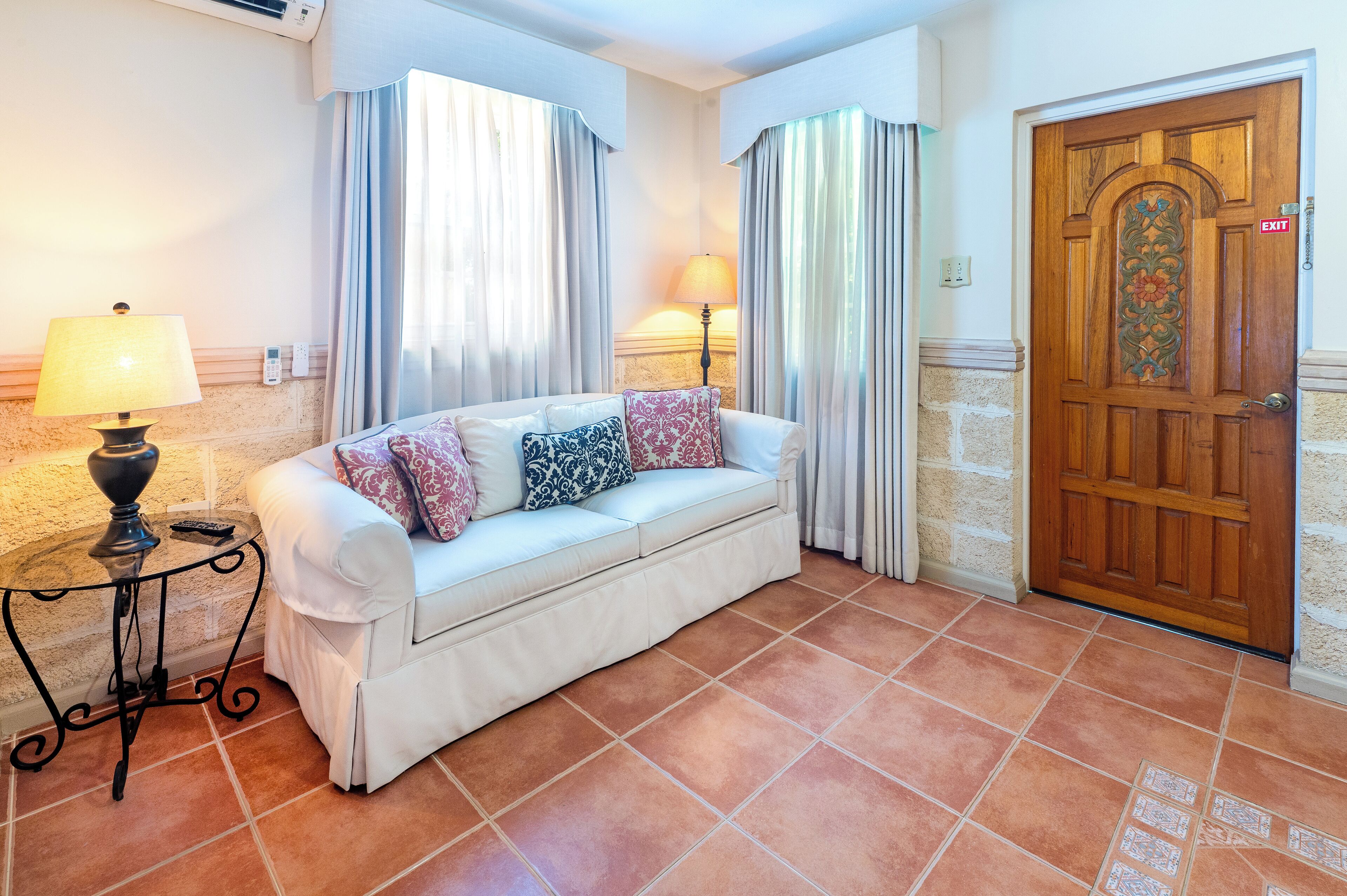 Quarto com sofá branco, duas luminárias, porta de madeira e piso de azulejos.