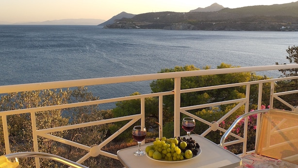 Ein Balkon mit Tisch für zwei Personen, mit Blick auf ein Gewässer und Hügel.