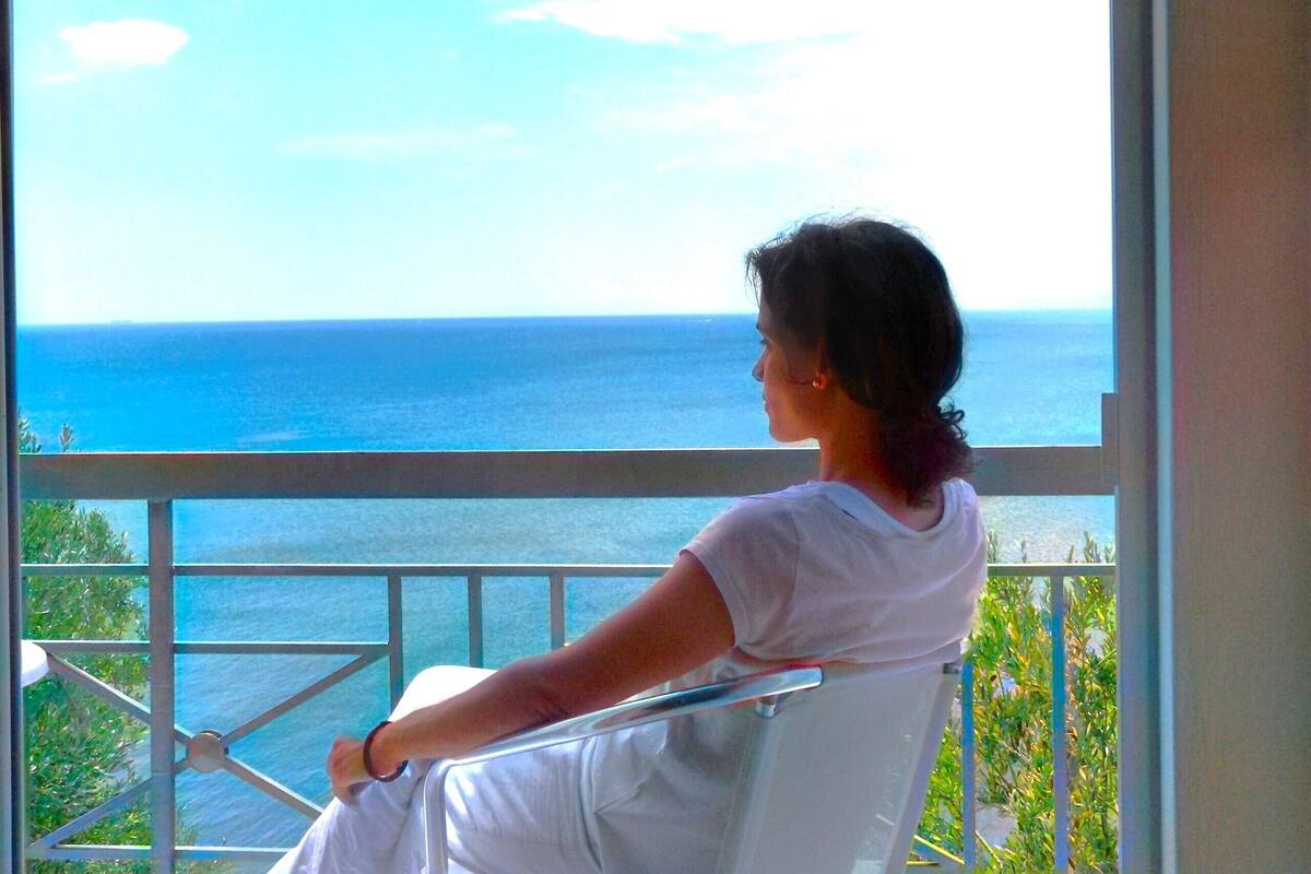 Eine Person sitzt auf einem Balkon mit Blick auf das Meer.