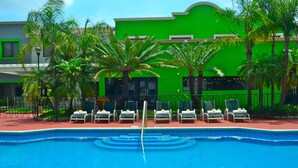 A swimming pool with lounge chairs and palm trees, surrounded by a building with a green facade.