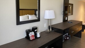 A hotel room with a large mirror, a bedside lamp, a coffee maker, and a minibar.