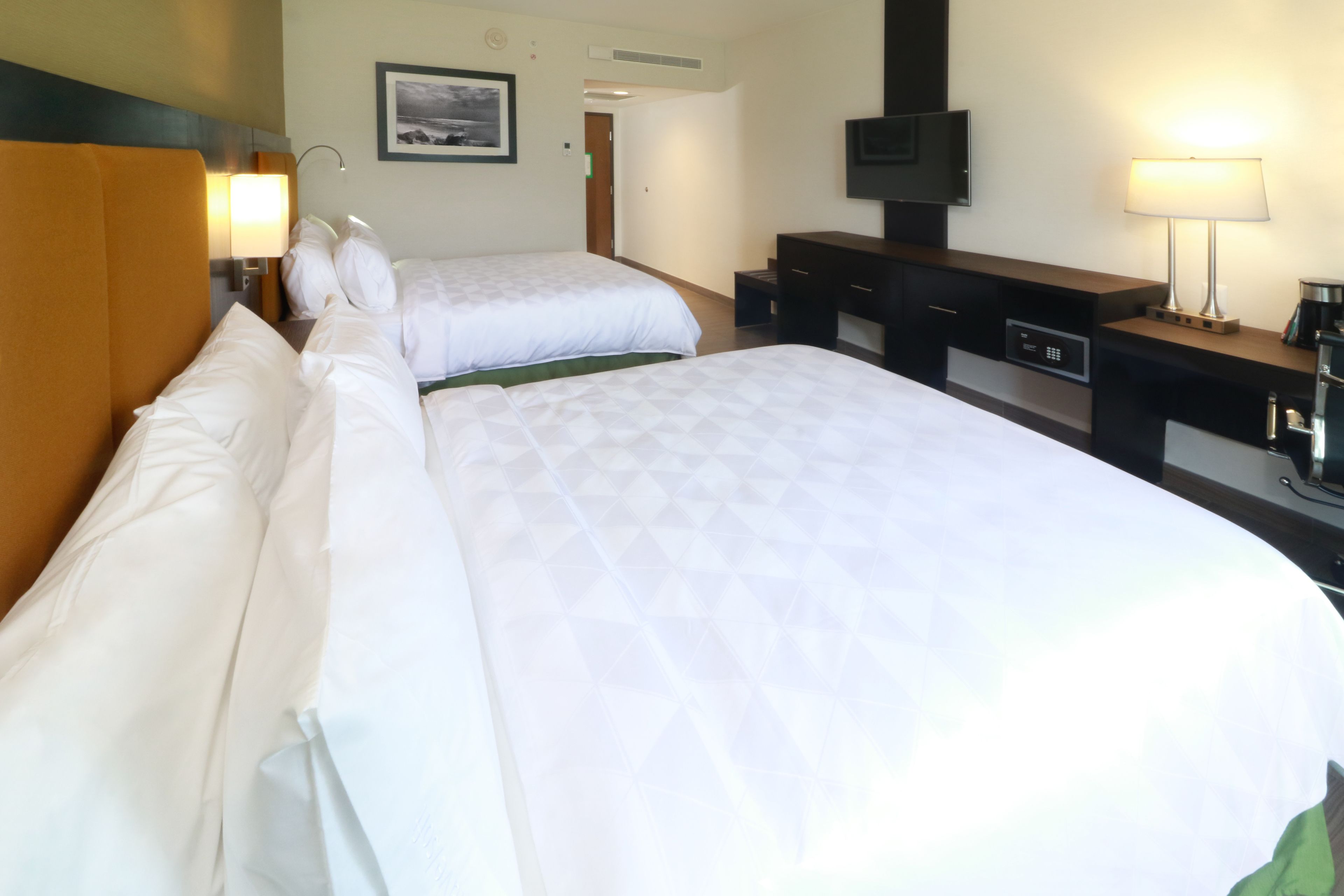 A hotel room with two beds, a desk, a television, and a lamp.