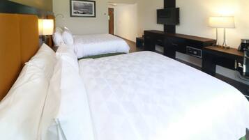 A hotel room with two beds, a desk, a television, and a lamp.