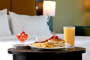 Un desayuno con tortitas, un vaso de zumo de naranja y un postre sobre una mesa.