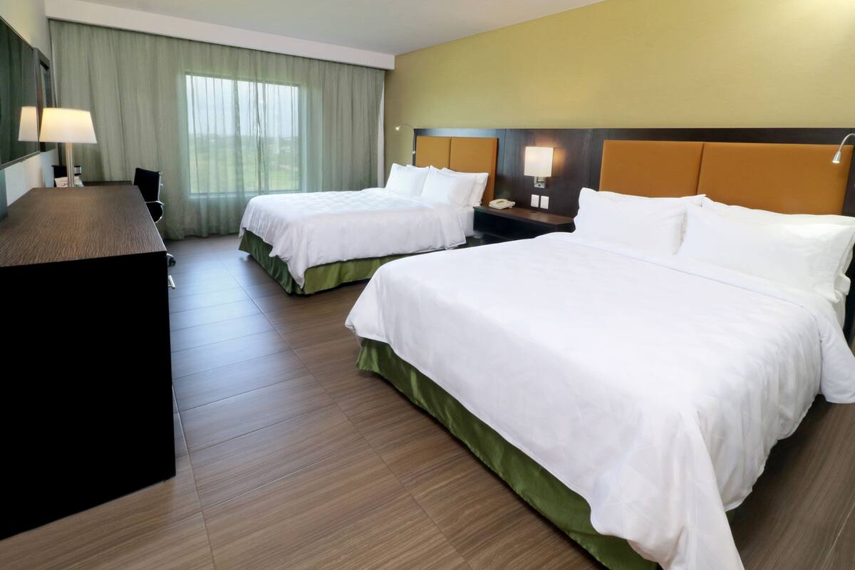 A hotel room with two beds, a desk, a lamp, and a telephone.