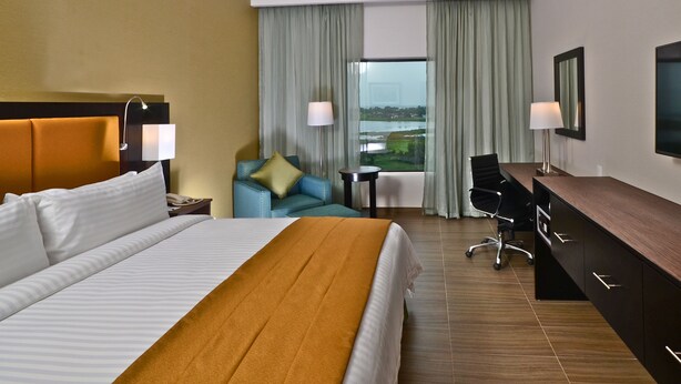 A hotel room with a large bed, a desk, a chair, and a view of a body of water.