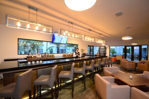 Zona de bar con una barra alargada, diversas opciones de asientos y una pantalla mostrando contenido.