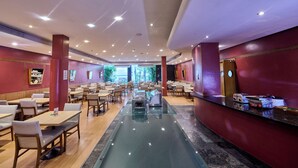 A spacious indoor area with multiple tables and chairs, a central pool, and a reception desk.