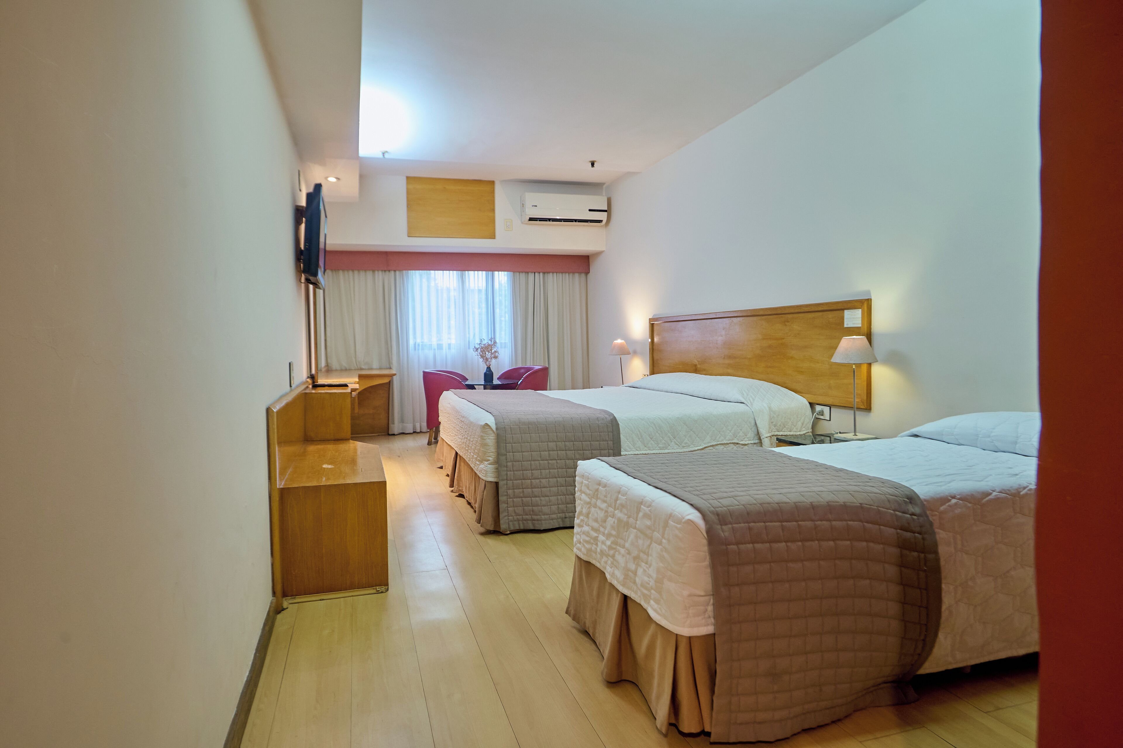 Een hotelkamer met twee bedden, een bureau, een stoel, een lamp en een airconditioning.