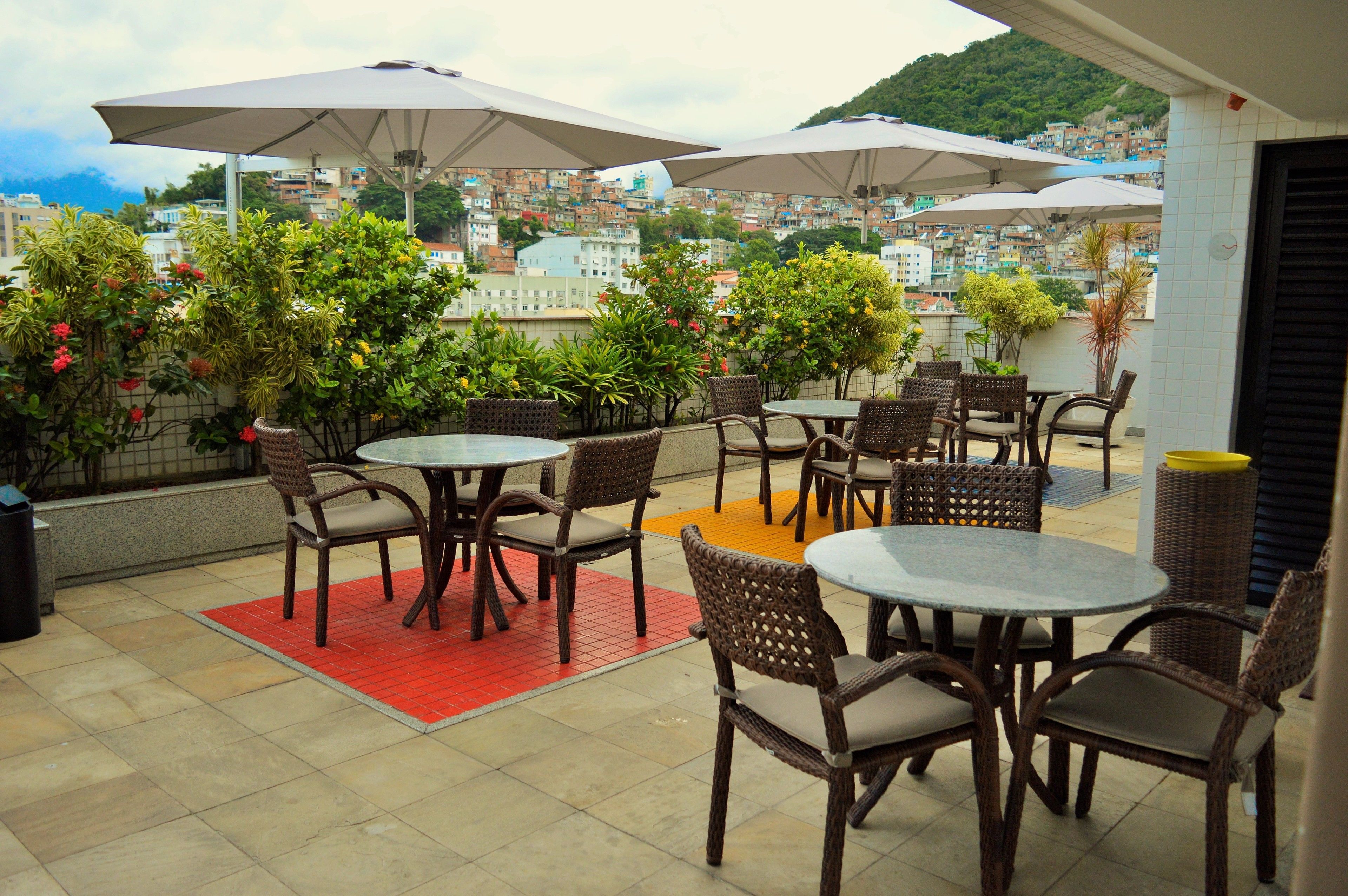 Une terrasse extérieure aménagée avec des meubles en osier et des parasols, offrant une vue sur un paysage urbain dense et vallonné.