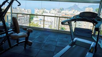 A gym with exercise equipment and a treadmill, overlooking a cityscape with buildings and mountains.
