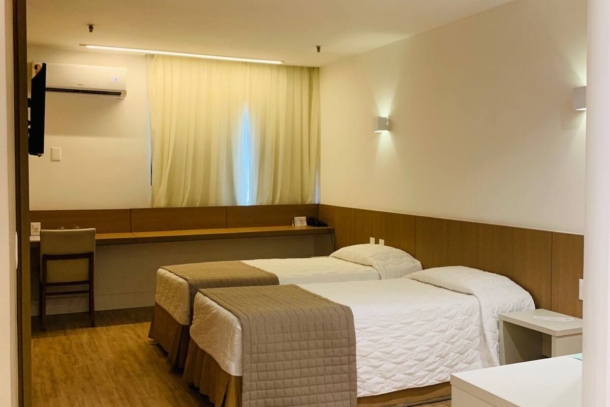 A hotel room with two beds, a desk, a chair, and a window with curtains.