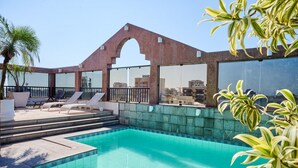 A rooftop pool area with lounge chairs, a palm tree, and a view of the cityscape.