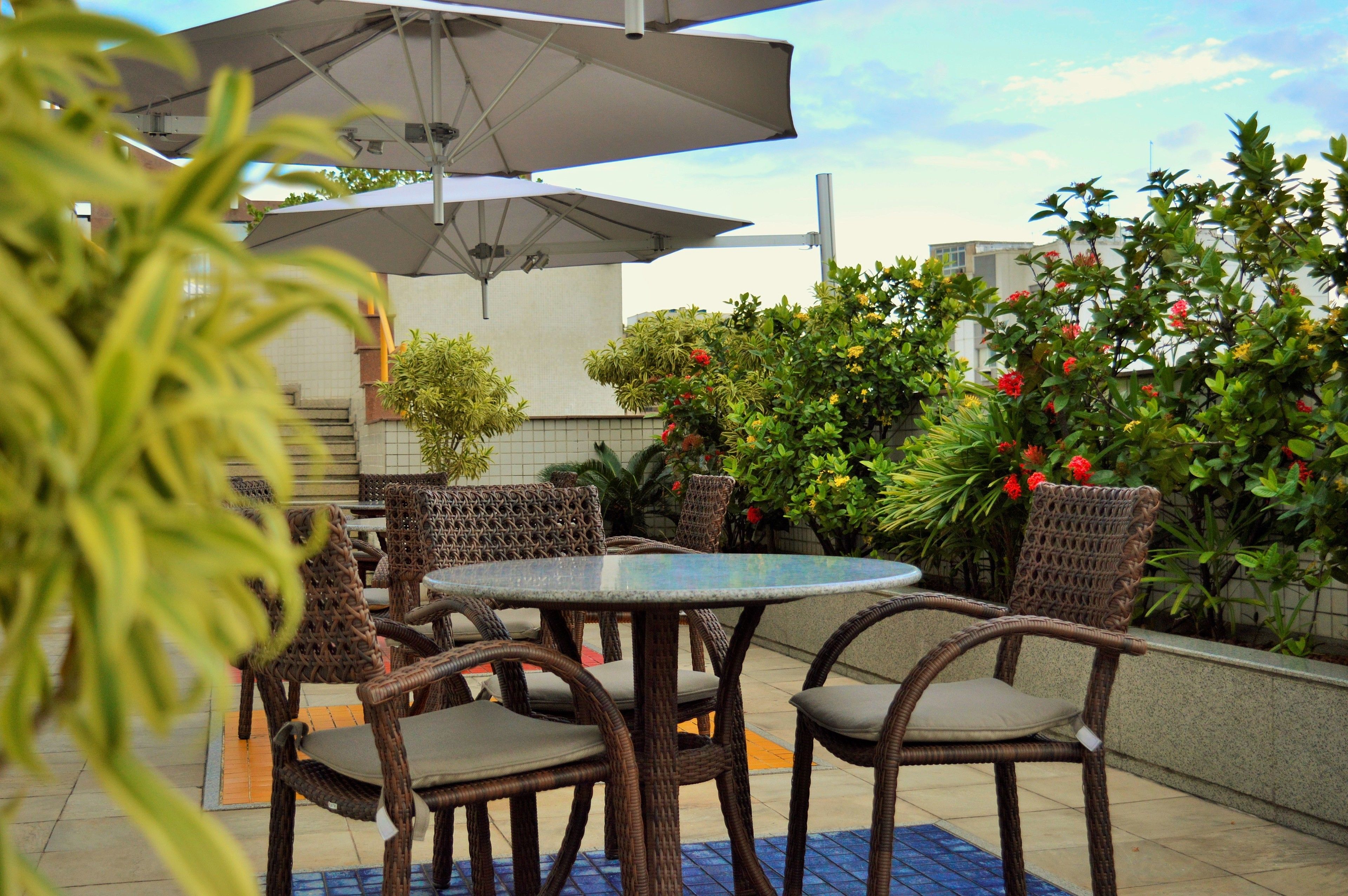 An outdoor patio area with wicker furniture, a round table, and umbrellas providing shade.