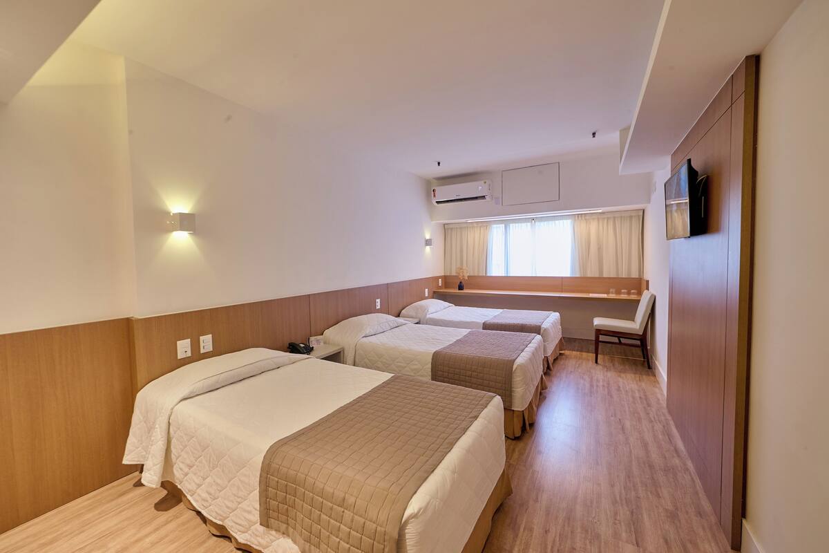 A hotel room with two beds, a desk, a chair, and a TV.