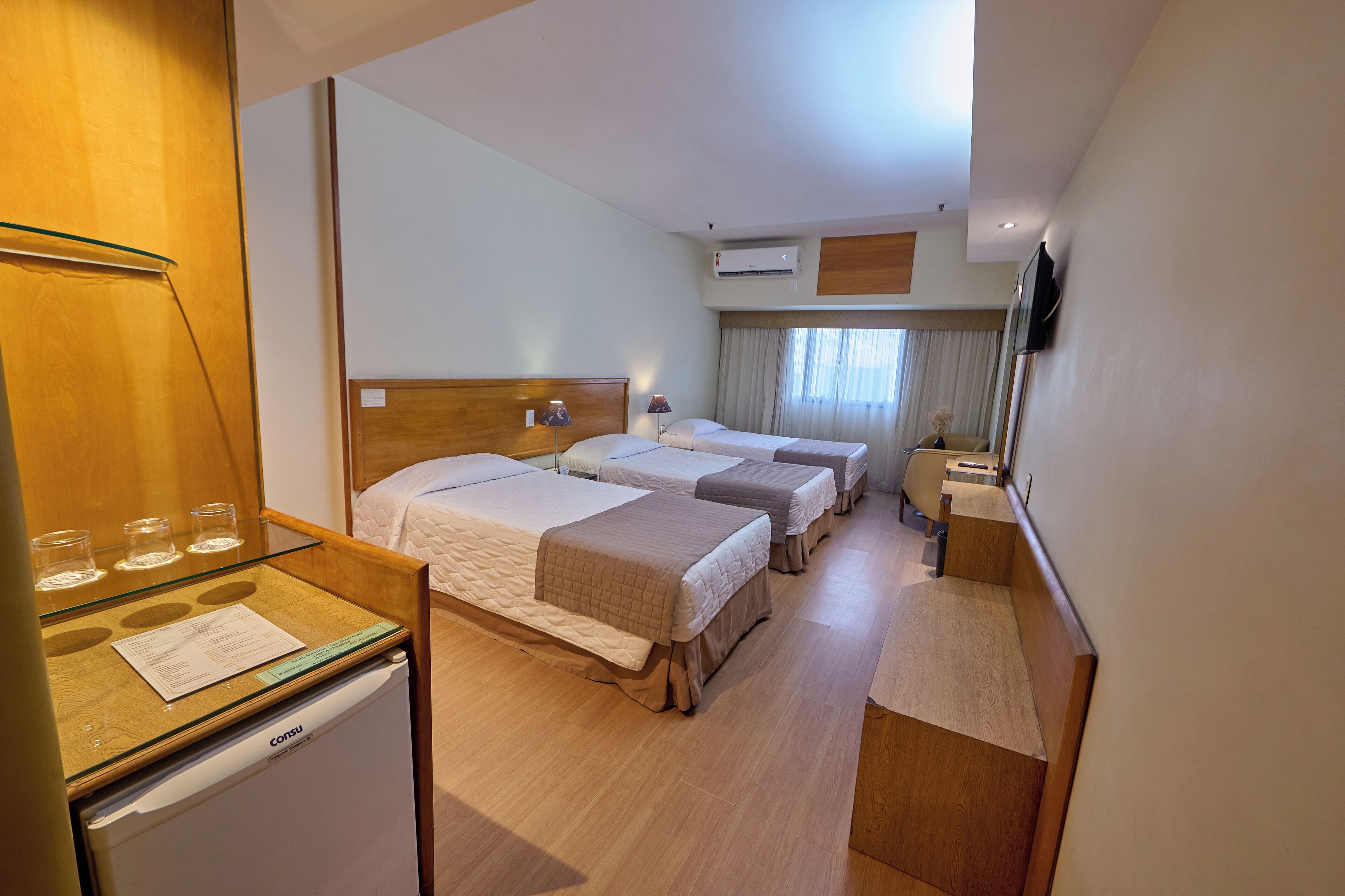 A hotel room with three beds, a small desk with a refrigerator, and a TV mounted on the wall.