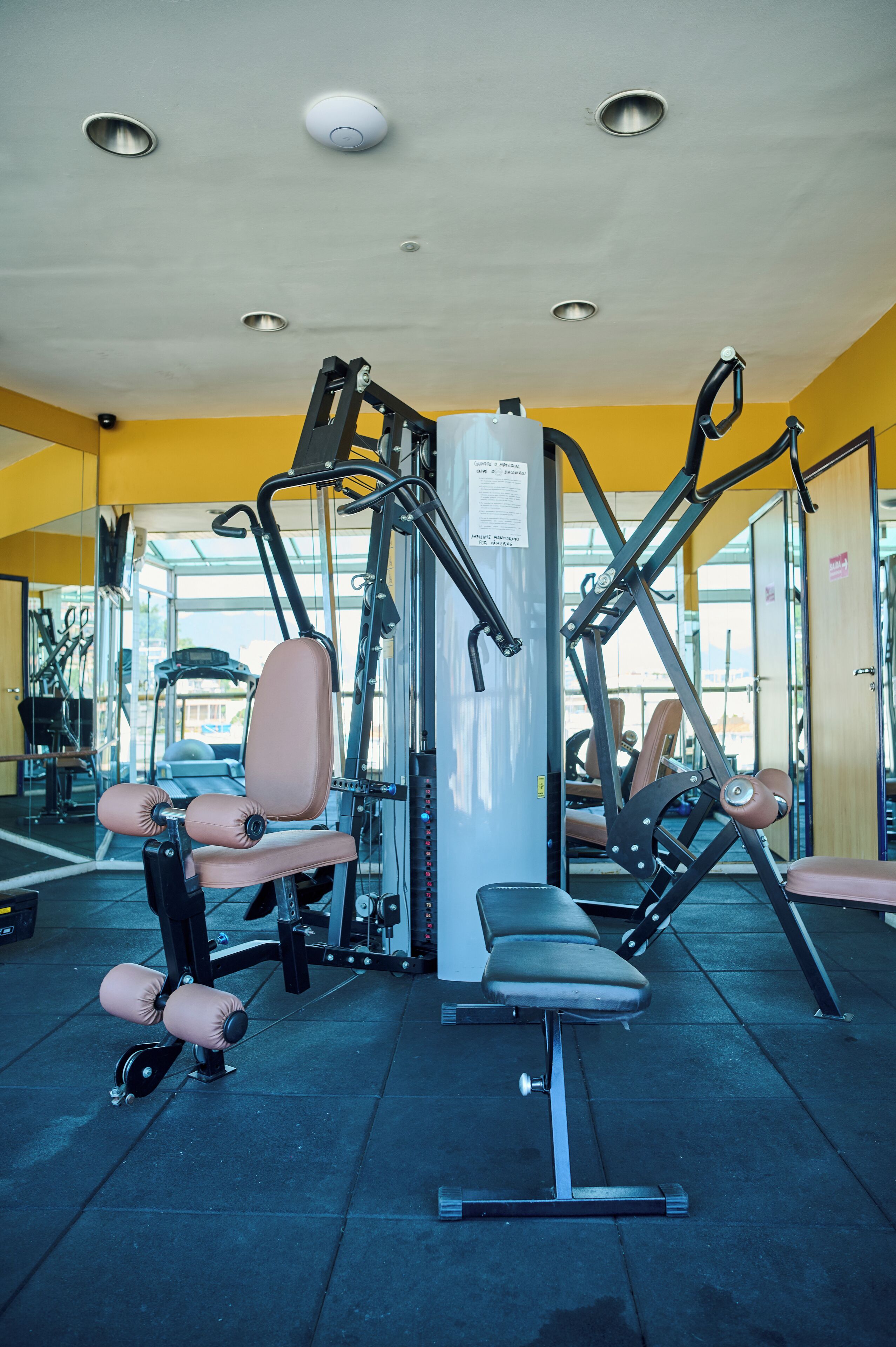 Ein Fitnessraum mit Trainingsgeräten, einer Bank und einem Wandspiegel.
