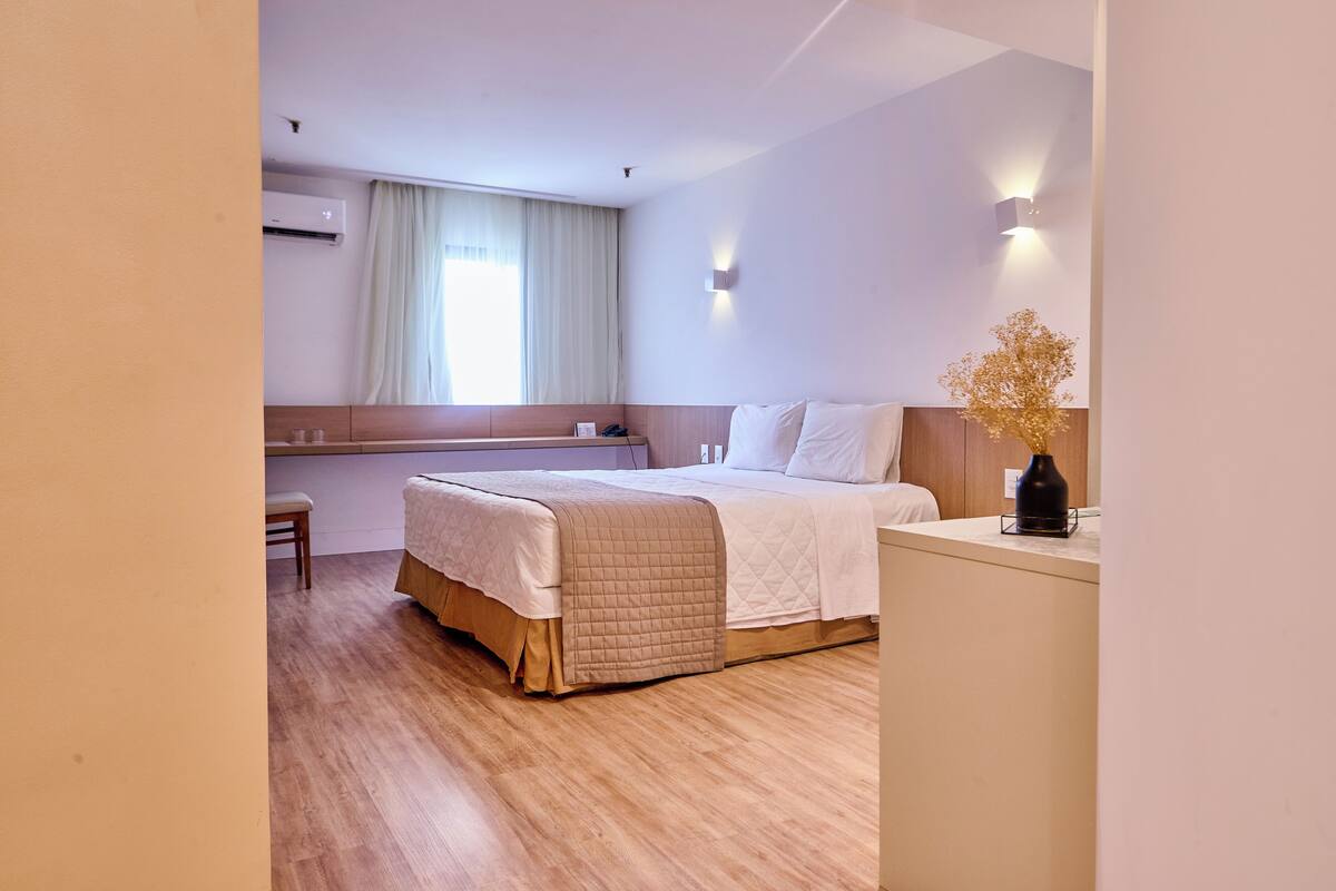 A hotel room with a bed, a desk, and a window with curtains.