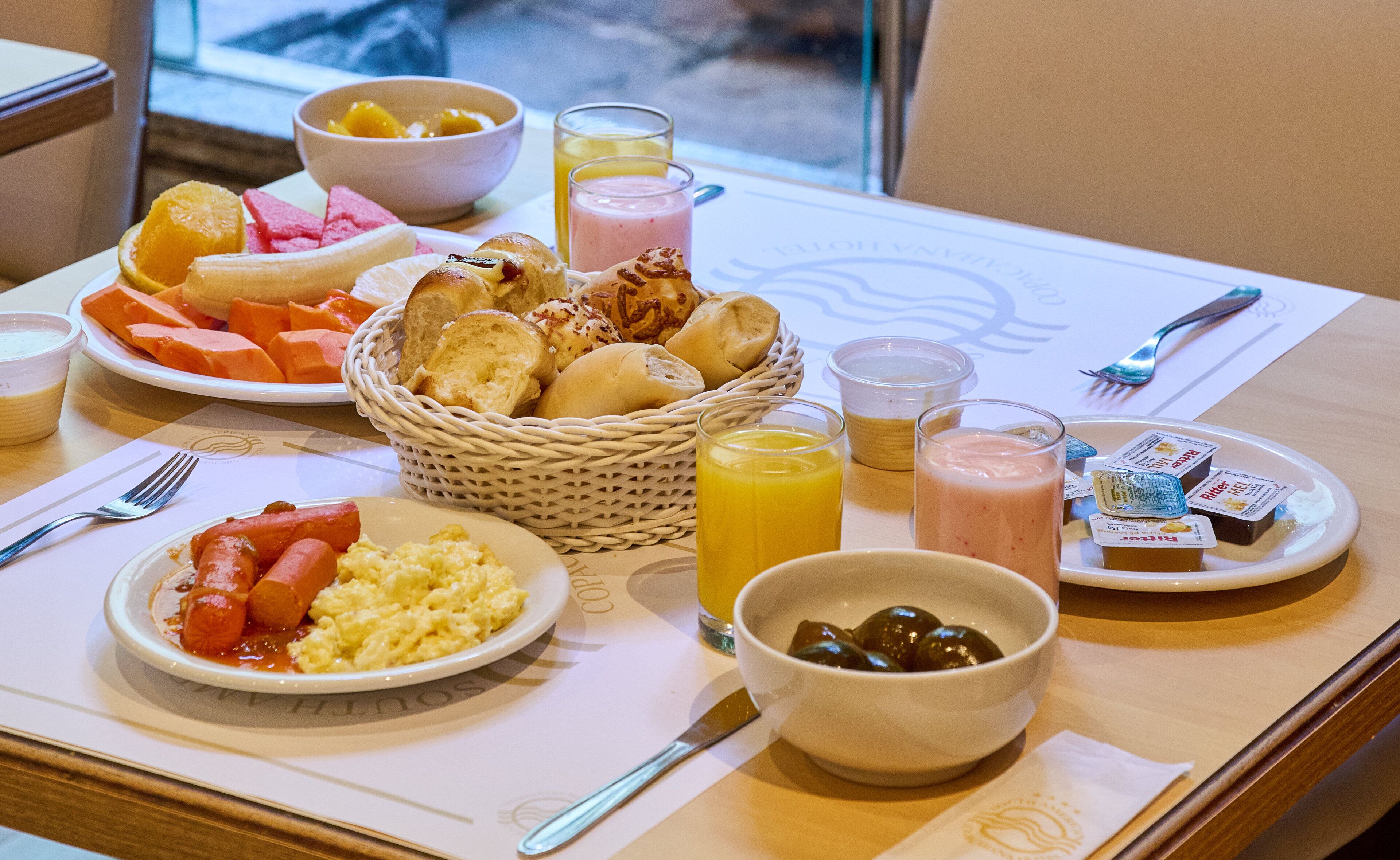 A breakfast buffet with various dishes, including scrambled eggs, sausages, and fresh fruits.