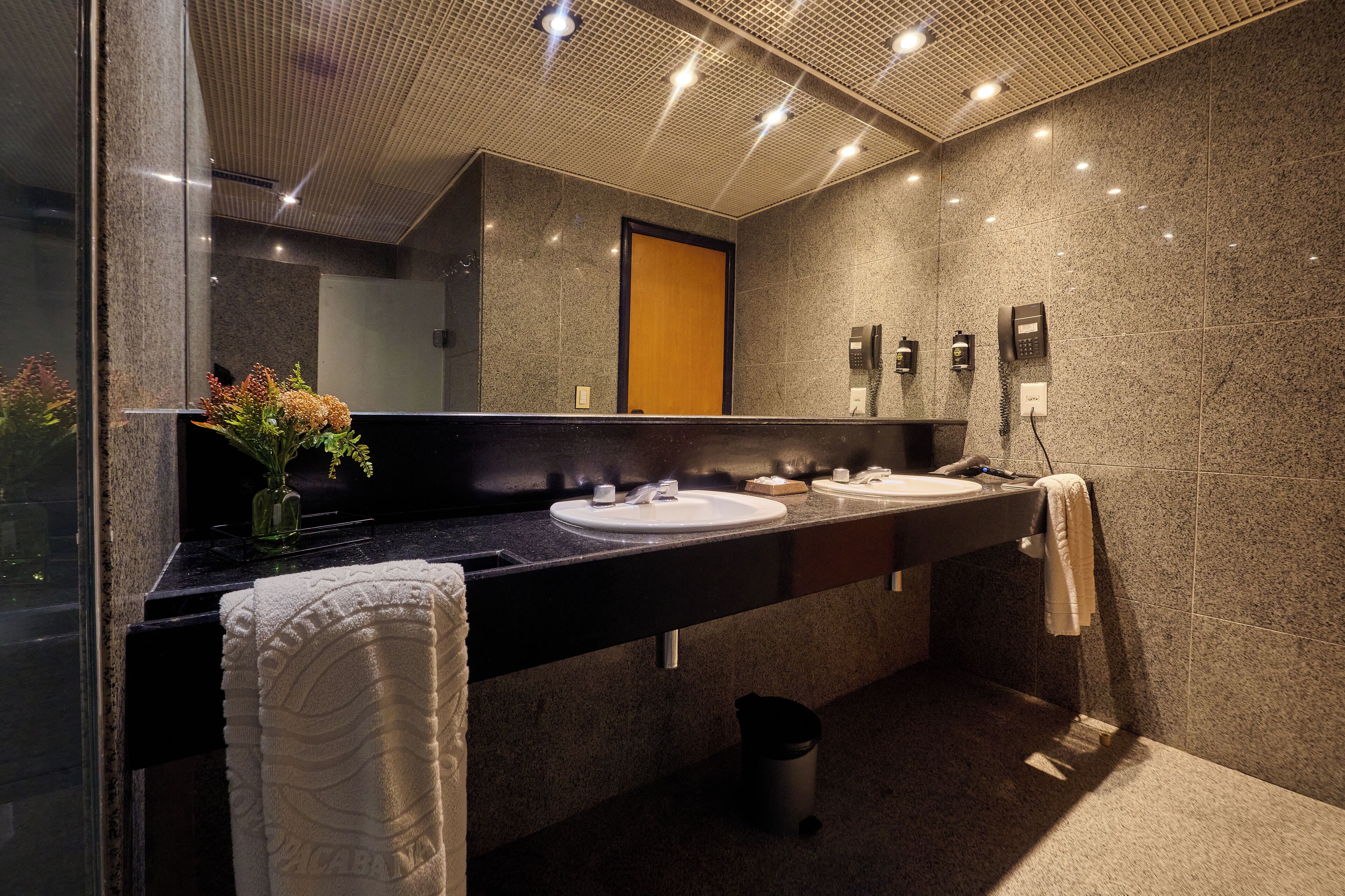A modern bathroom with two sinks, a mirror, and a trash bin.