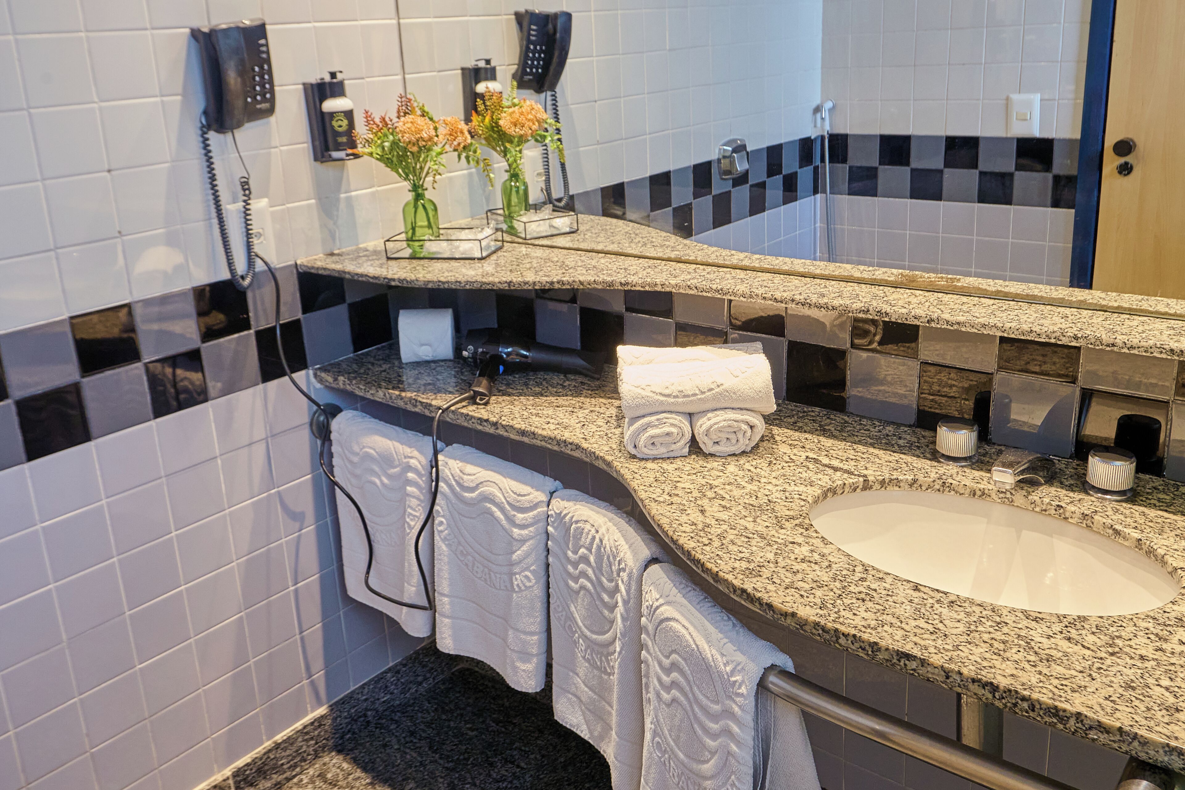 Ein Badezimmer mit einer Granit-Arbeitsfläche, einem weißen Waschbecken und zwei Vasen mit Blumen.