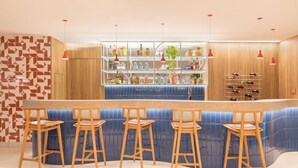 A bar area with wooden bar stools, a blue bar counter, and shelves with bottles. - Copa Sul Hotel (Rio de Janeiro)