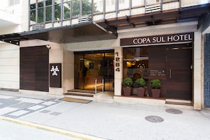 The exterior of the Copa Sul Hotel, featuring a modern facade, large entrance doors, and potted plants at the entrance.