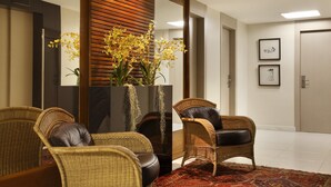 A reception area with wicker chairs, a large mirror, and a vase of yellow flowers. - Copa Sul Hotel (Rio de Janeiro)