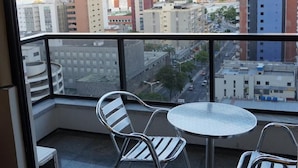 A balcony with a table and chairs, overlooking a cityscape with various buildings.