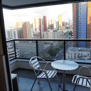 A balcony with a table and chairs, overlooking a cityscape with various buildings.