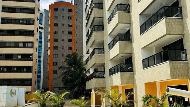 A swimming pool surrounded by high-rise buildings with balconies, a clear sky, and some palm trees.