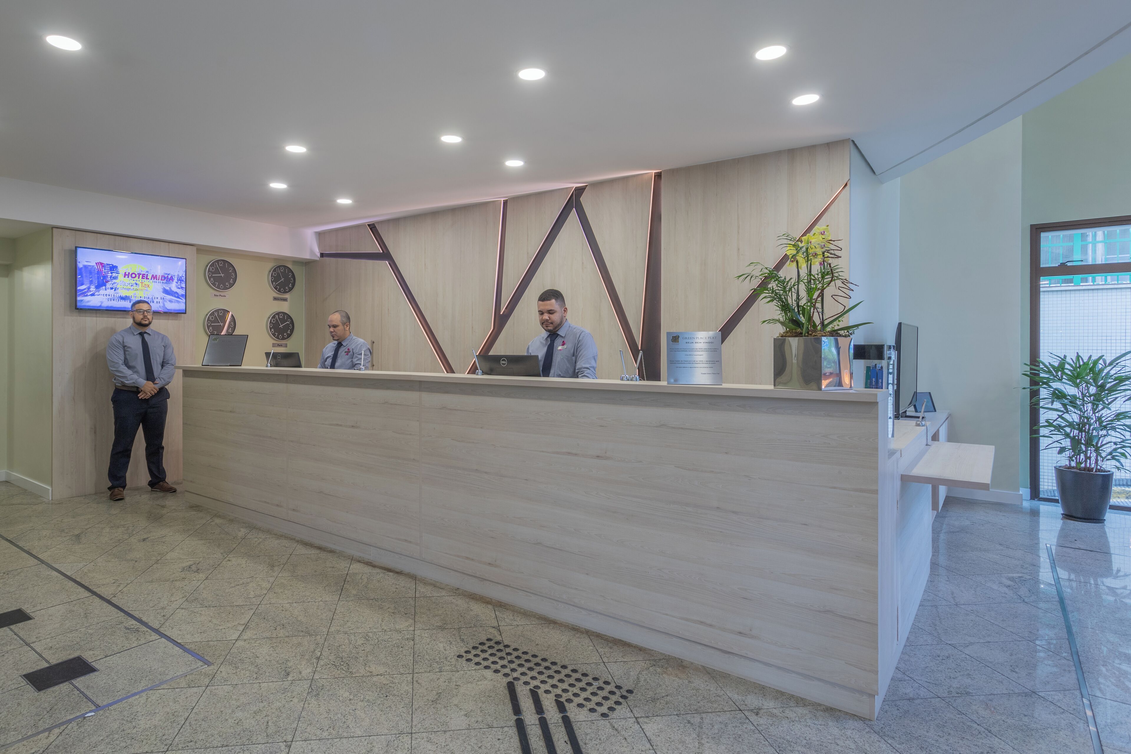 A hotel reception desk with a modern design, a digital screen displaying hotel information, and a clock.