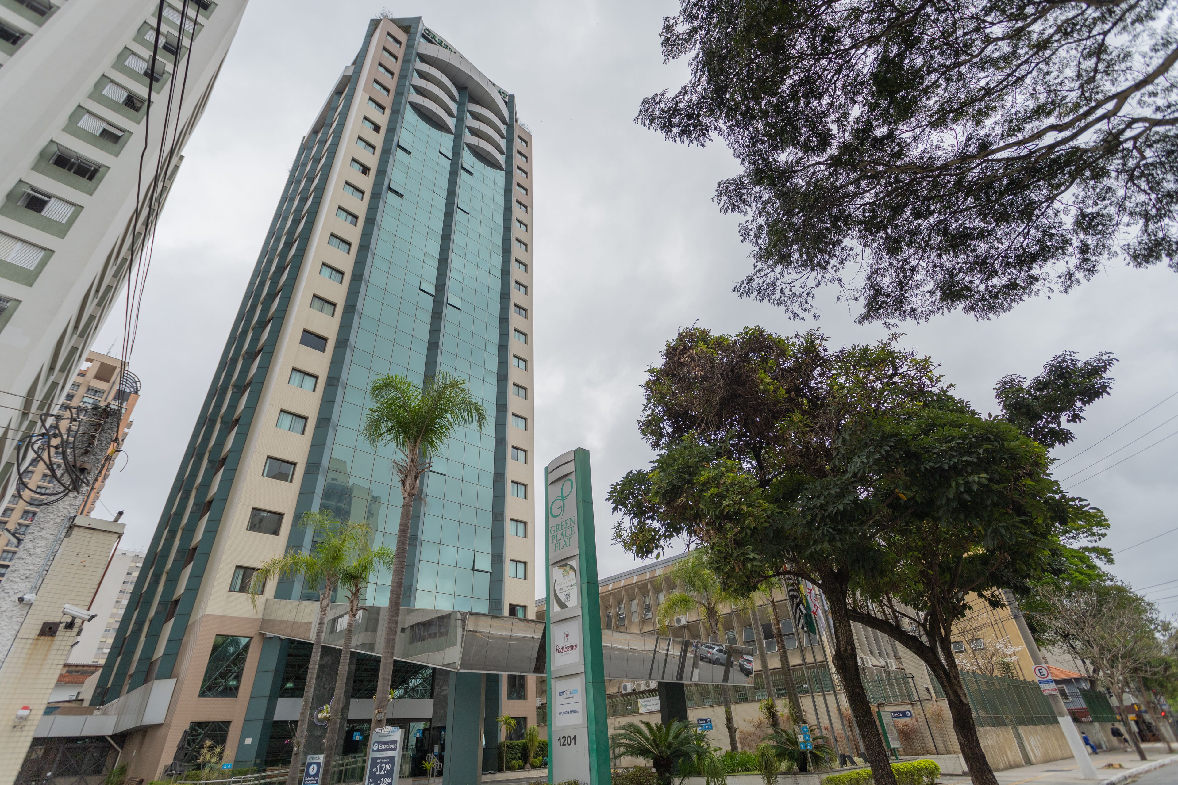 A modern high-rise building with a glass facade, surrounded by trees and other buildings.