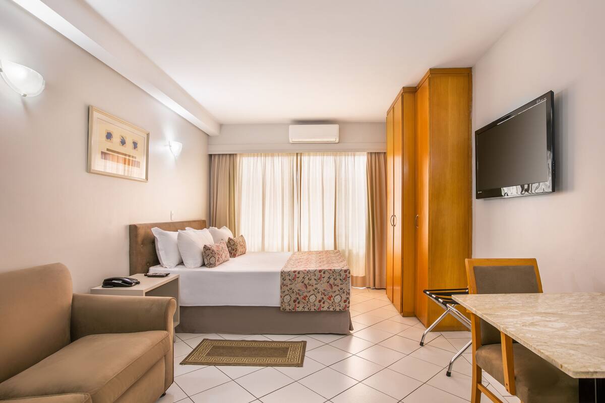A hotel room with a bed, a desk, a chair, a TV, and curtains.