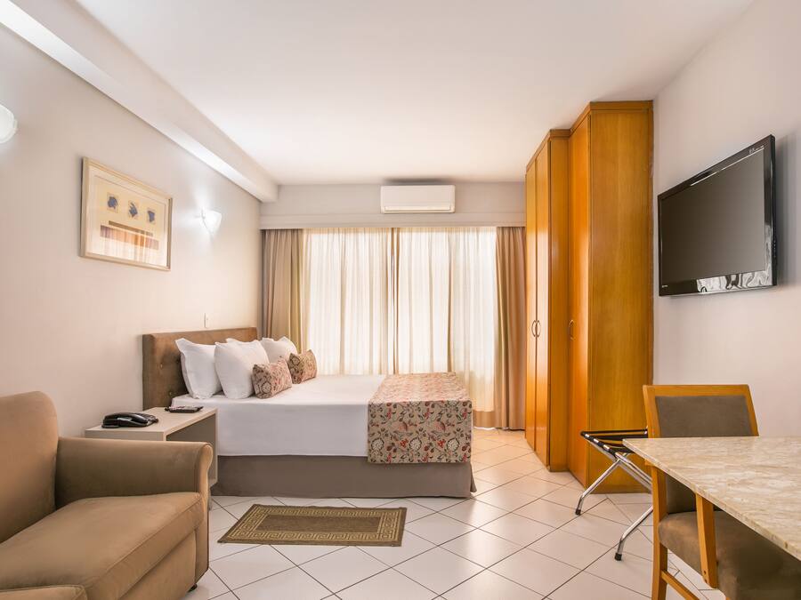 Ein Hotelzimmer mit Bett, Schreibtisch, Stuhl, Fernseher und Vorhängen.