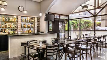 Zona de bar con varias botellas de licor, un reloj y un ventanal con vista a zonas verdes.