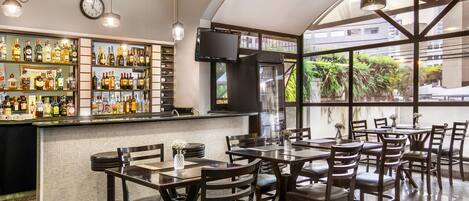 Zona de bar con varias botellas de licor, un reloj y un ventanal con vista a zonas verdes.