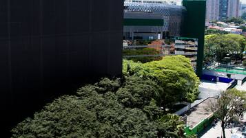 A high-rise building with a modern glass facade, a large green structure, and a dense tree area in the foreground.