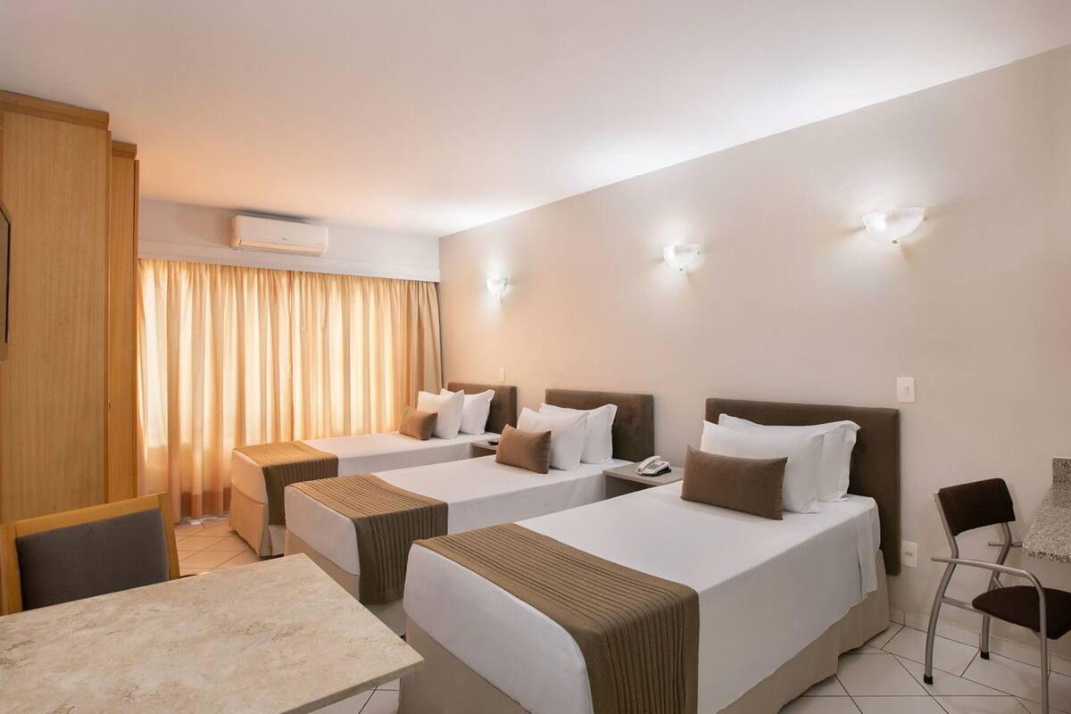 A hotel room with two beds, a desk, a chair, and a TV.