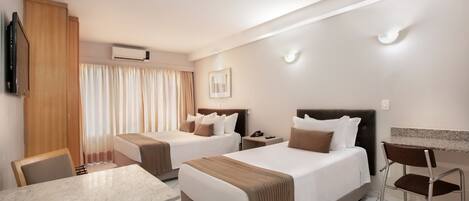 A hotel room with two beds, a desk, a chair, a TV, an air conditioner, and a window with curtains.