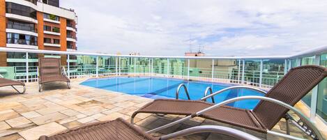 A rooftop pool area with lounge chairs and a glass balustrade.