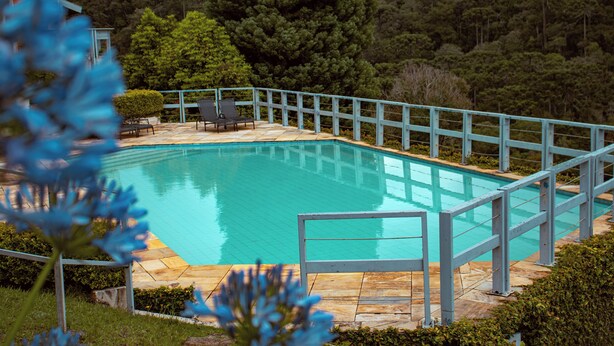 A swimming pool with a blue railing, surrounded by a stone deck and a view of a forested hillside. - Plaza Inn Week Inn (Campos do Jordão)
