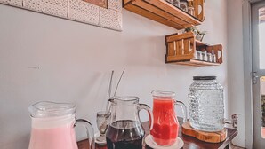 A kitchen counter with three pitchers of different colored beverages, wooden shelves above holding jars and a small plant, and a decorative wall hanging. - Plaza Inn Week Inn (Campos do Jordão)