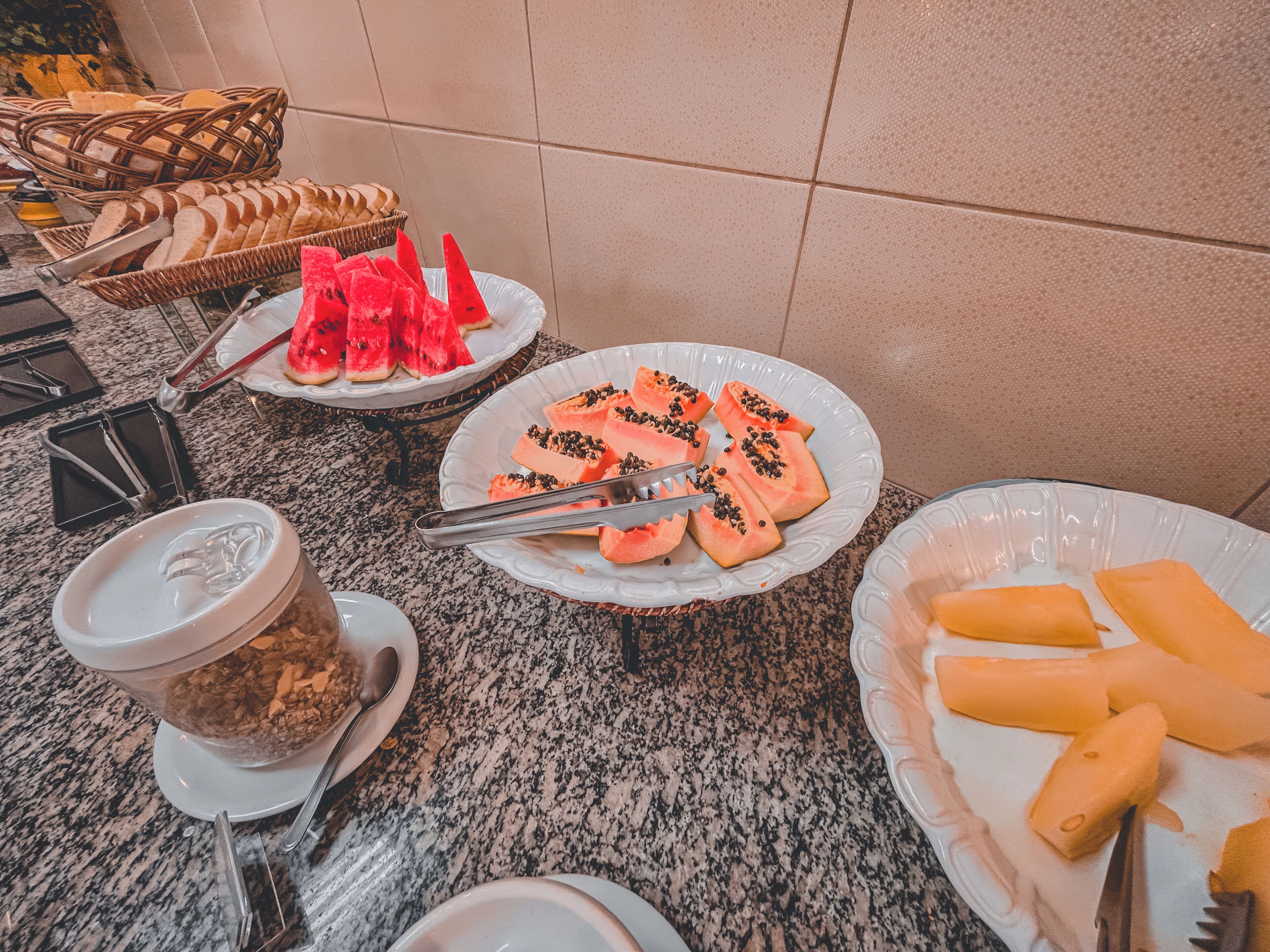 A buffet table with various food items including watermelon slices, bread, and other fruits.