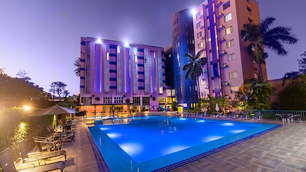 A swimming pool with lounge chairs and umbrellas, surrounded by a building with multiple floors and balconies. - Falls Galli Hotel (Foz do Iguaçu)