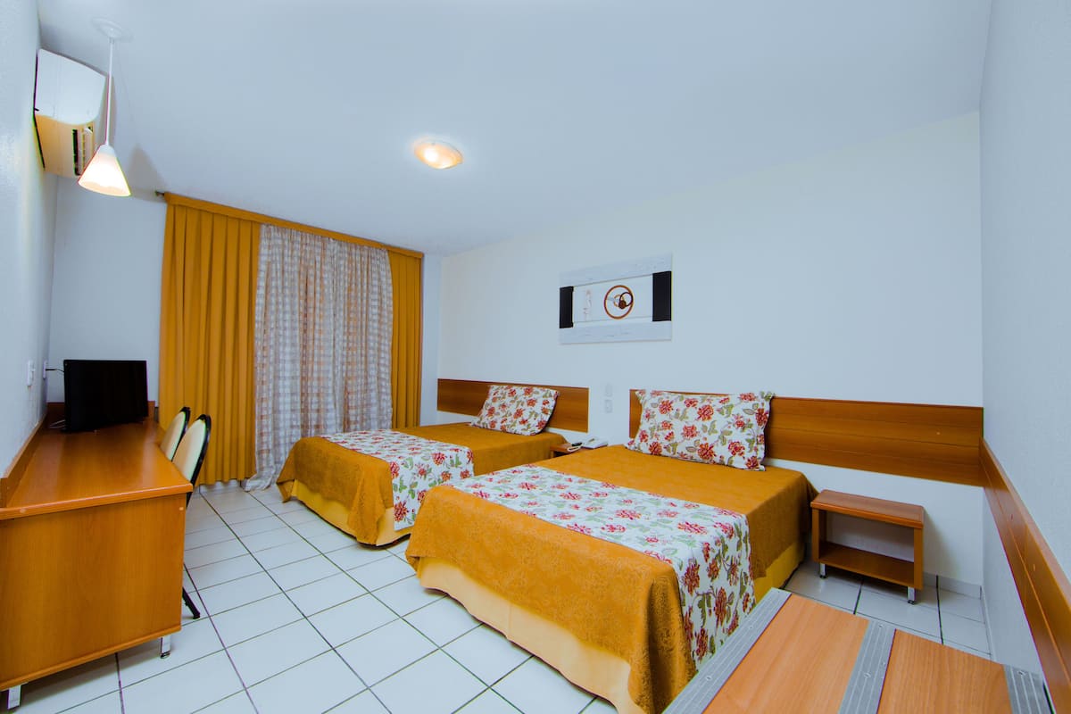 Une chambre d’hôtel avec deux lits, un bureau, une chaise, une télévision et une petite table.